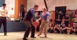 Il attrape sa main pour danser mais reste concentré sur l'homme à la chemise blanche derrière eux