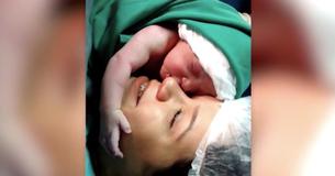 Pasgeboren baby houdt gezicht van moeder stevig vast