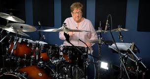Eine Großmutter zeigt am Schlagzeug ihre Skills mit einem Cover von einem Disturbed Hit