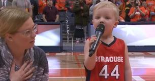 Un enfant se tient courageusement debout dans une foule de milliers de personnes pour chanter son hymne national