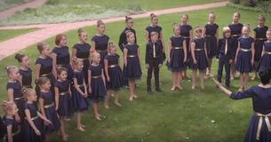 Kinderkoor zingt een eigen versie van  'You Raise Me Up' door Josh Groban in een open veld.
