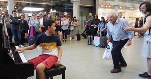 Twee mannen onderbreken jongetje dat piano speelt in het Londense St. Pancras treinstation om het verzoeknummer "Bohemian Rhapsody" te vragen.