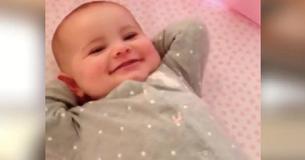Un papa regarde son bébé heureux, allongé et souriant dans son berceau le matin et le filme