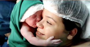 Pasgeboren baby houdt het gezicht van de moeder stevig vast.