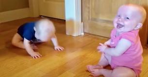 Tweeling brengt elkaar aan het lachen, terwijl filmende moeder haar lachen niet in kan houden om baby in blauw